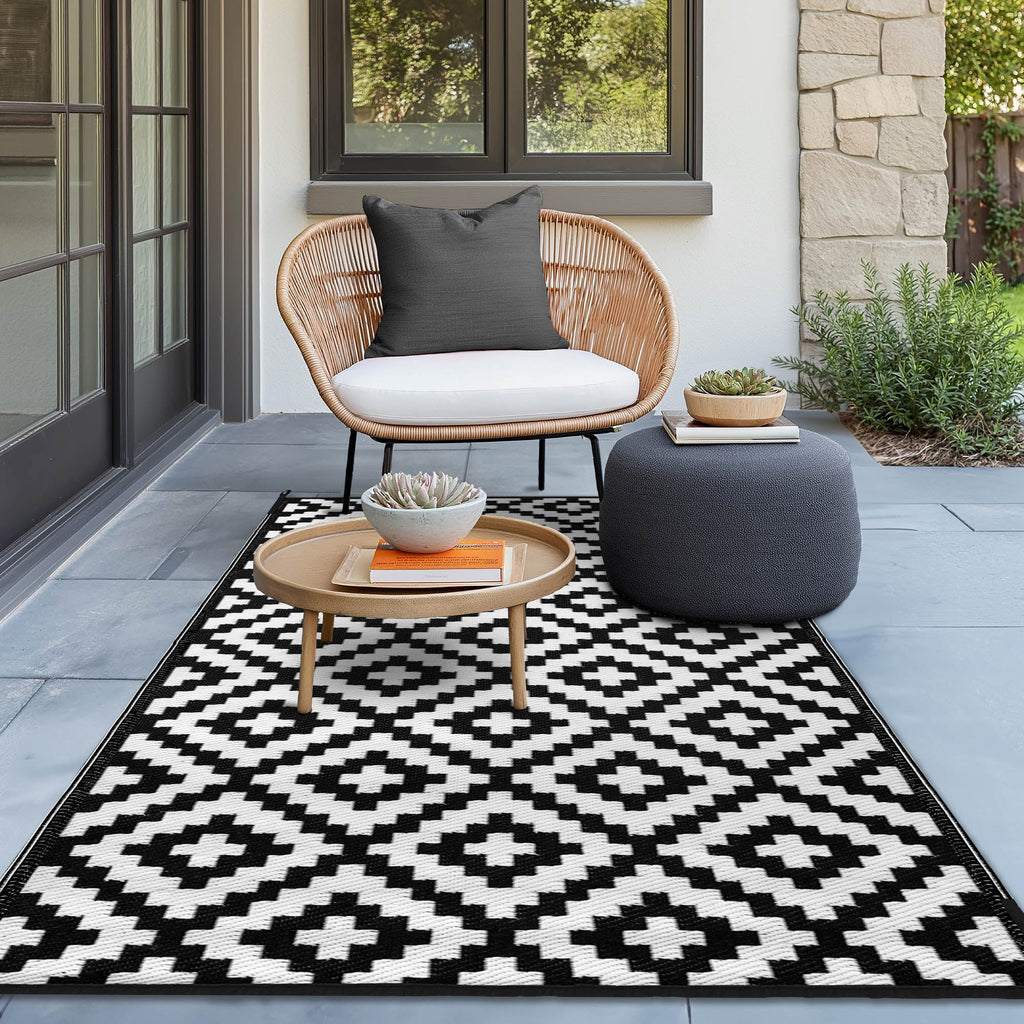 tylish outdoor patio setup featuring Green Decore Bliss Outdoor Recycled Plastic Rug in Black and White (120 x 180 cm), with bold geometric pattern, paired with a rattan chair, black cushion.