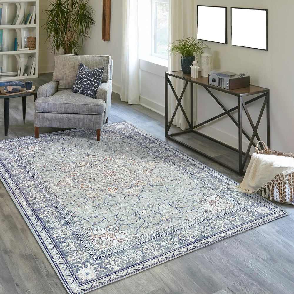 Vernal Adora Grey & Copper Machine Washable Rug featuring an intricate floral and vine border design with a detailed central medallion, styled in a modern living room with a grey armchair, console table, and natural light from a nearby window. 