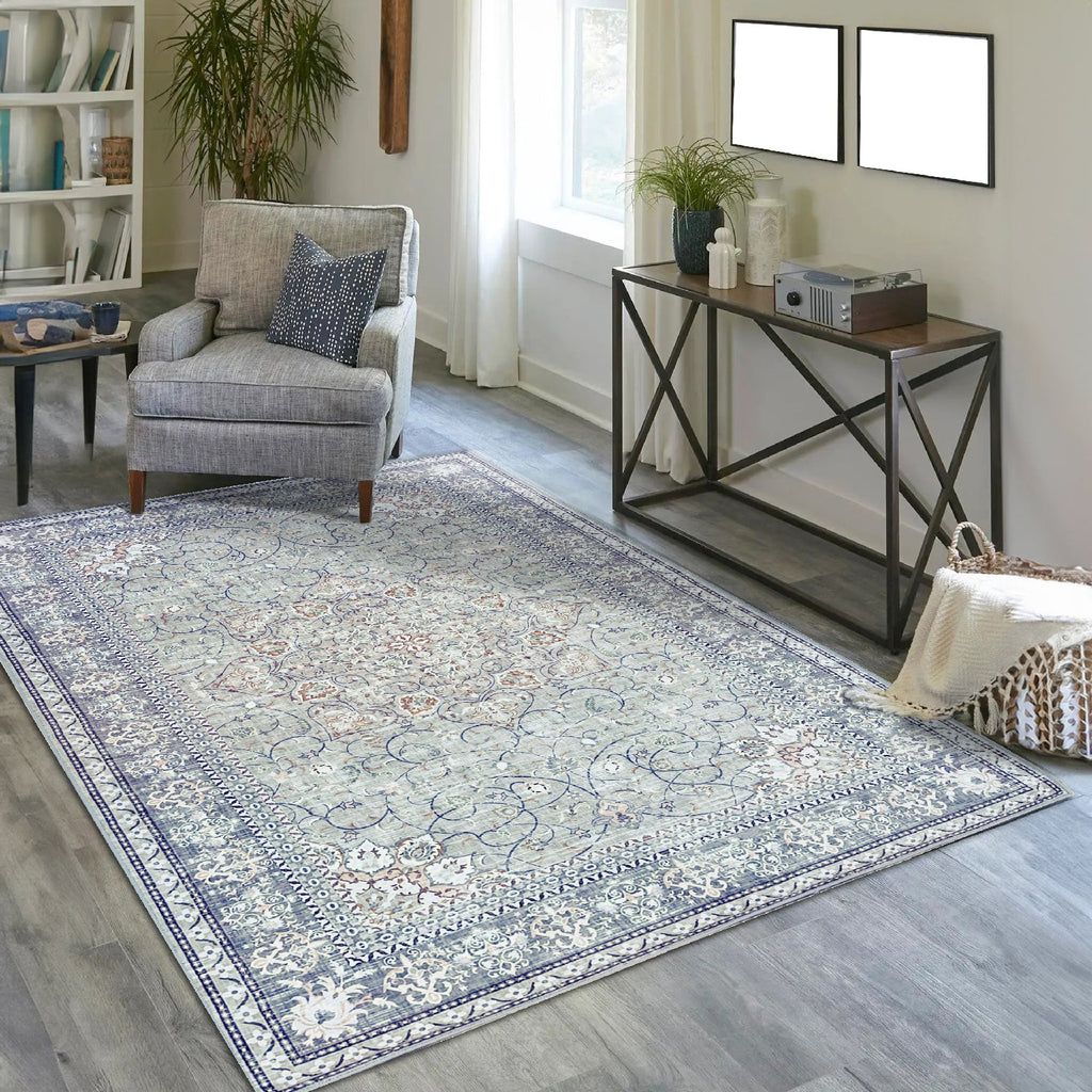 Vernal Adora Grey & Copper Machine Washable Rug featuring an intricate floral and vine border design with a detailed central medallion, styled in a modern living room with a grey armchair, console table, and natural light from a nearby window. 