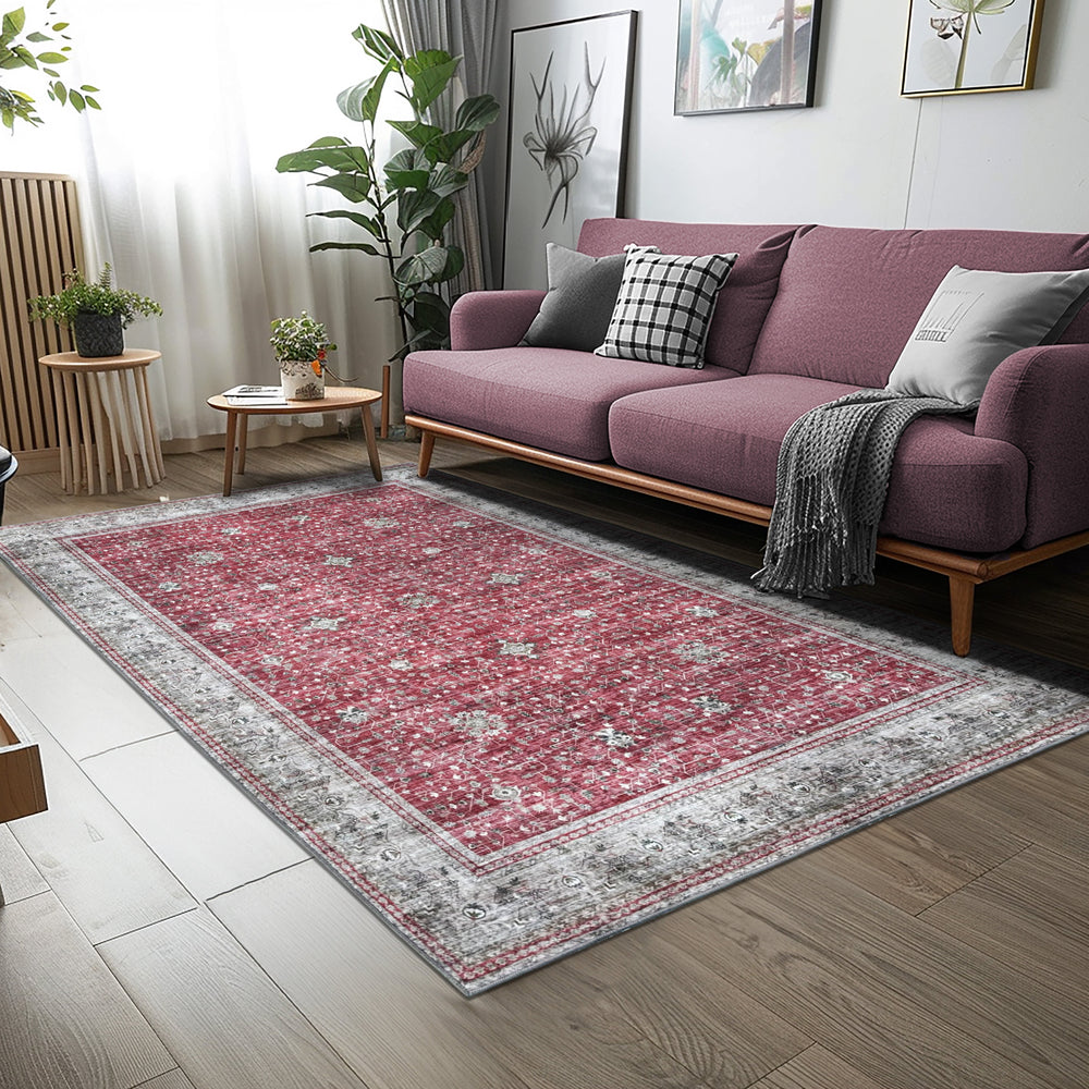 Green Decore Vernal Inge Rust & Beige Machine Washable Rug placed in a modern living room with wooden flooring, a mauve sofa, and indoor plants. The rug features a vintage floral pattern with a distressed grey border, adding warmth and charm. 