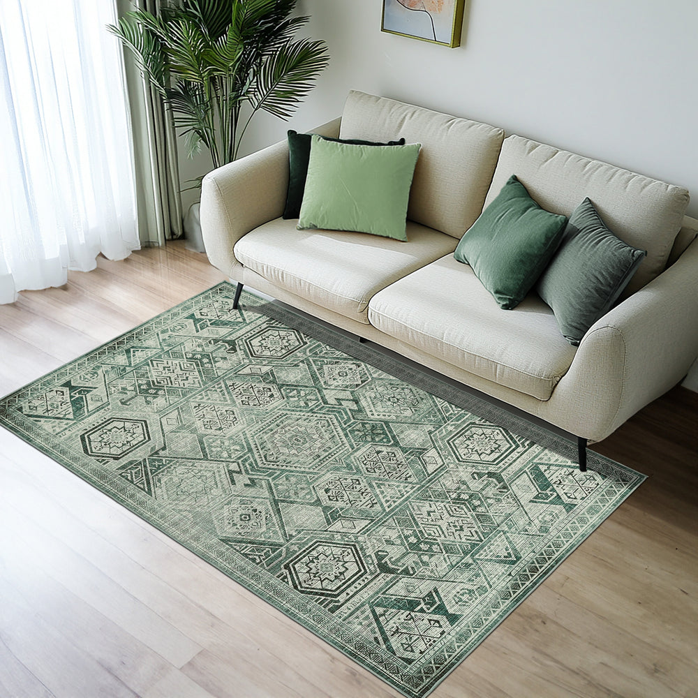 Green Decore Vernal Freya Sage Green Machine Washable Rug with intricate geometric patterns in soft green tones, placed in a modern living room with a beige sofa, green cushions, wooden flooring, and natural light filtering through sheer white curtains. 