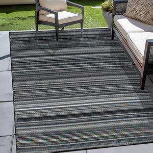 Black Outdoor Rug with a sleek striped design, placed on a tiled patio beside cushioned chairs and a sofa, perfect for enhancing modern outdoor lounging areas.
