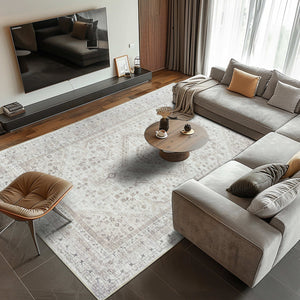 Modern living room featuring the Vernal Senglea Beige, Taupe & Cream Machine Washable Rug beneath a large sectional sofa and round wooden coffee table, adding a touch of elegance and warmth to the neutral-toned space.
