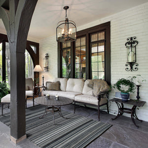 Black Outdoor Rug with elegant striped pattern placed on a covered patio, paired with cushioned wrought iron seating and classic décor, ideal for stylish and durable outdoor comfort.
